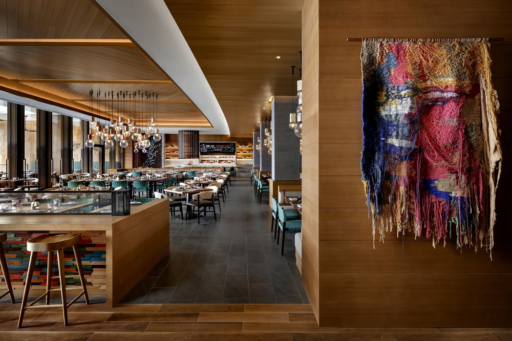 A modern restaurant interior featuring a long dining area with wooden accents